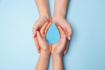 Human hands holding water drop isolated on white wooden background. Top view. Eco friendly living,...