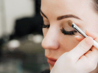 brush with eyeshadow in the hands of a makeup artist at the eyes of a girl in a beauty salon