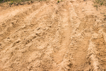 Sand texture background. Climbing sandy road after rain with traces of skidding cars. Mud and sand off-road background. Challenging track for car racing.