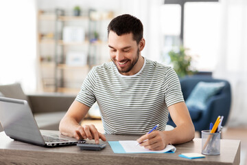 remote job and business concept - happy smiling man with papers, calculator and laptop computer...