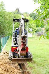 Workman using a mini digger to excavate a hole in the garden. Czech republic, Europe.
