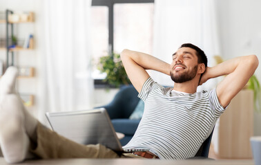 remote job and business concept - happy smiling man with laptop computer resting feet on table at home office