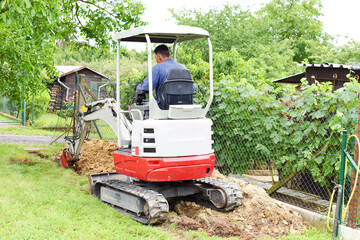 Workman using a mini digger to excavate a hole in the garden. Czech republic, Europe.