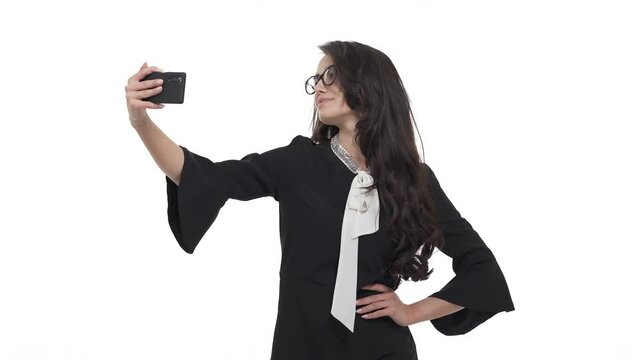 Portrait of young Caucasian woman in glasses taking selfie, posing on Smartphone camera. Isolated on white background.