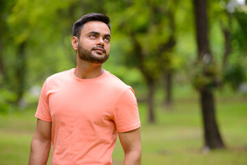 Fototapeta na wymiar Young handsome bearded Indian man at the park