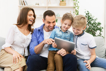 Fototapeta premium Parents And Kids Using Tablet Sitting On Sofa At Home