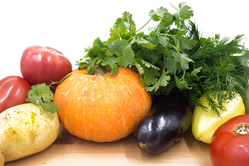 Fresh vegetables on a wooden cutting board, closeup: Pumpkin, potatoes, green onions, dill, tomato, parsley. Healthy food, vegan food.