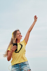 young blonde woman using yellow headphones in front of the beach on a summer cloudy day