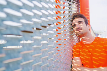 Portrait of caucasian sad man leaning on metal fence with hands crossed looking thoughtful, young caucasian male runner taking break after active training with copy space area for text your message