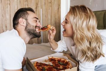Happy loving couple relaxing on a bed with pizza
