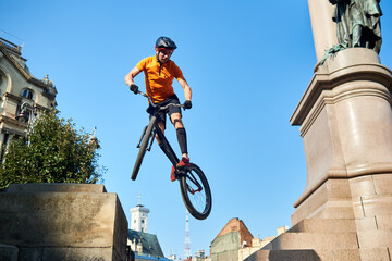 View from below extreme man holding a sport bike and hanging in air. Cyclist looking down when doing trick. Concept of trick.
