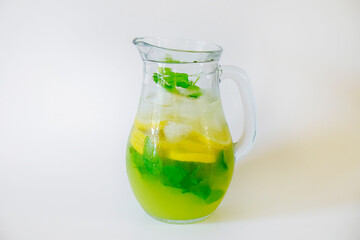 Vintage jug with refreshing non alcoholic mojito drink with lemon slices, mint leaves and ice. Studio shot of iced lemonade isolated on white background, close up, copy space.