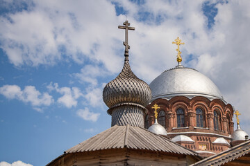 old wooden church with wooden dome and cross in front of orange brick church with silver dome and golden cross