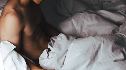 a naked man lying in bed covered with white sheets