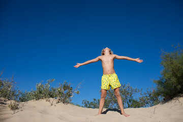 Young teen boy in yellow swim shorts posing on a sand hill at the beach. Copy space.