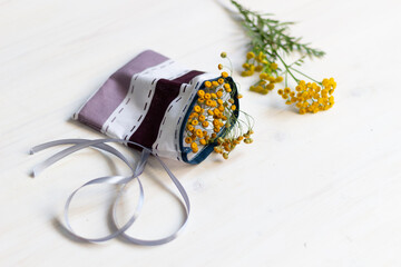 Cotton sachet packet with dry tansy flowers and fresh herb on white wooden background