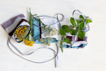 Cotton sachet bag with dry tansy flowers, yarrow, mint  and fresh herb on white wooden background