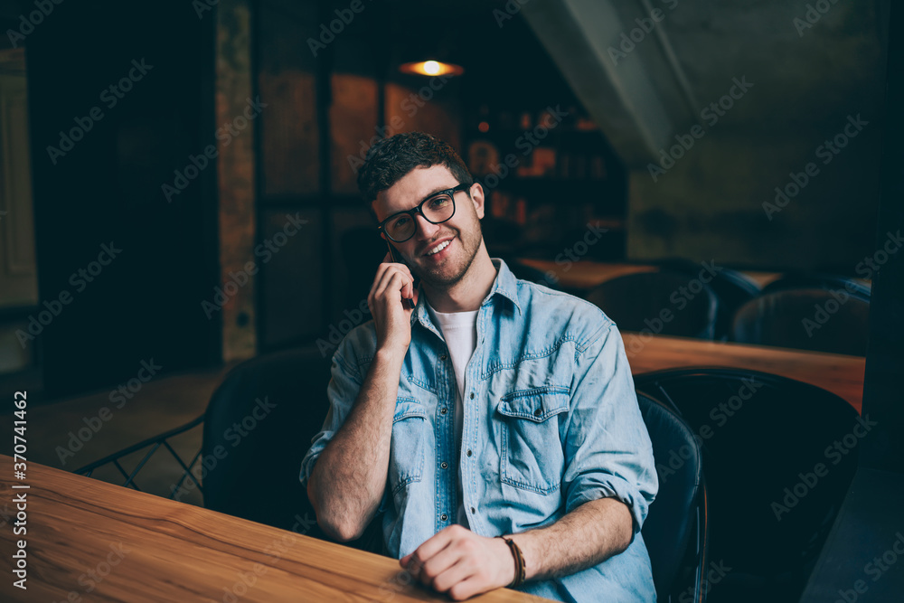 Poster portrait of happy cheerful hipster guy looking at camera and consulting with colleague vie telephone