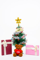 Fototapeta na wymiar Teddy bear with love sign and Christmas presents under Christmas tree with Merry Christmas writing