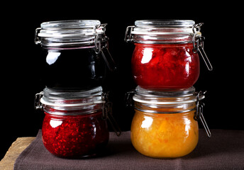 Bilberry, strawberry, orange and raspberry jams in glass jars against the black background