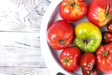 Tomatoes of different sorts in a bowl on the white wooden table. Top view