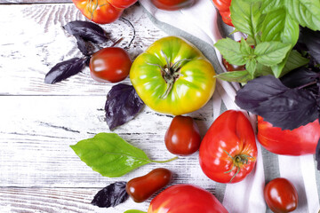 Different tomatoes and basil leaves scattered around the white wooden table