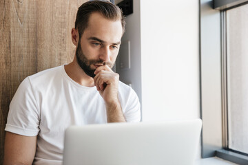 Image of young concentrated man using laptop and smiling