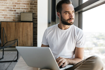 Image of concentrated man working with laptop while sitting near window