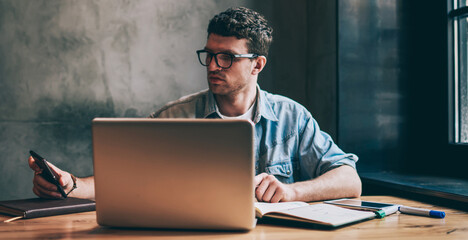 Handsome male it professional checking time on smartphone device and updating notification indoors,...
