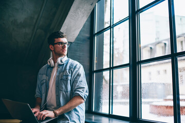 Young contemplative male freelancer pondering on program code holding laptop during free time at...