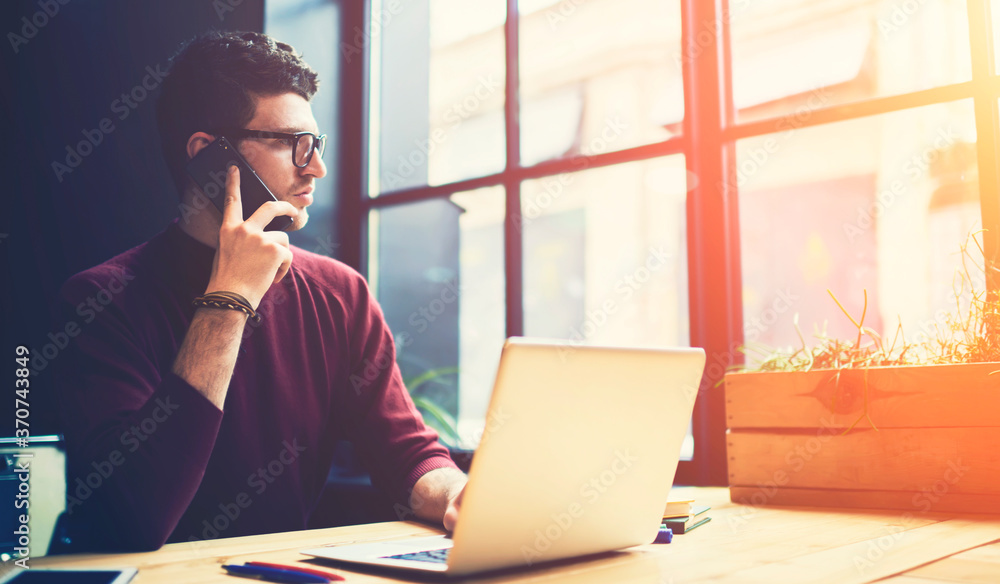 Poster handsome serious entrepreneur having mobile conversation with colleague on telephone using applicati