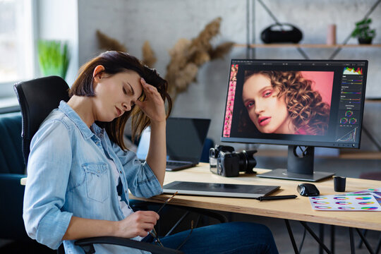 Portrait of tired graphic designer working overtime in office. Stressed worker have eye strain symptoms. Retoucher workplace in photo studio. Burnout and overwork concept. Creative agency.