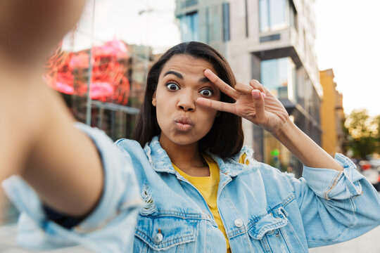 Image of african american woman gesturing peace sign and taking selfie