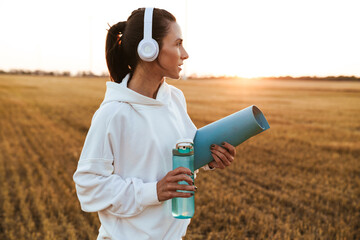 Image of nice sportswoman drinking water while holding yoga mat