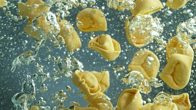 Throwing tortellini, pasta into boiled water in pot shooting with high speed cinematic camera at 1000 fps.