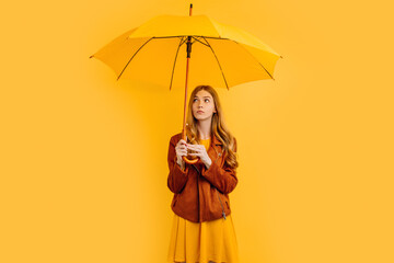 Beautiful girl with a yellow umbrella, with a thoughtful face, on a yellow background