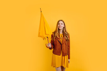 beautiful girl, in a bright yellow dress and autumn jacket, stands with a yellow umbrella on an...