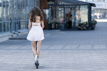 Naklejka premium A girl in a dress who rides an electric scooter in the city