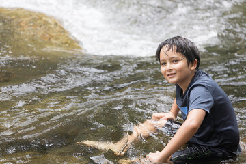 A portrait of an elementary school boy sitting on a rock in a fast-flowing stream at Khiri Wong village. Khiri Wong village is a famous village of natural tourism in Thailand.