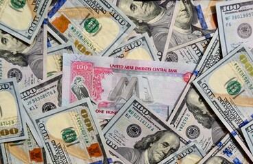 UAE national banknote on top of USA national currency, top view of mixed American dollars banknotes. UAE and USA paper money. 100 Dirhams and US dollars exchange rate. USD, AED