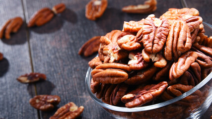 Bowl with pecan nuts on wooden table.