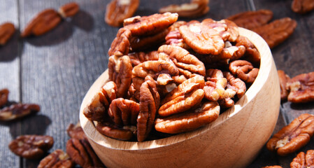 Bowl with pecan nuts on wooden table.