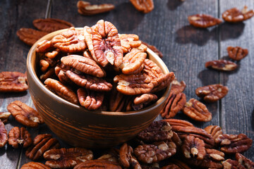 Bowl with pecan nuts on wooden table.