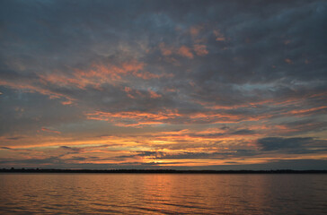 Canadian sunset over a beautiful lake showing a horizon full of colours in pink, gold, orange and teal clouds.