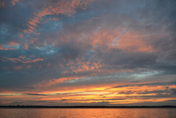 A glorious sunset over a calm lake in Canada, revealing bold colours in the clouds and lake of pinks, golds, oranges and teals.