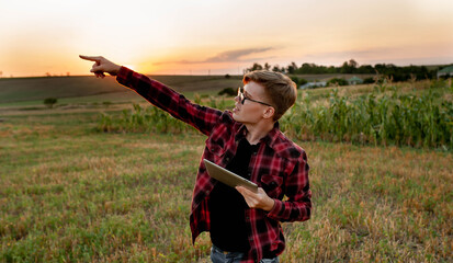 
Farmer with tablet at sunset in the field shows with his hand to the side, agriculture management concept