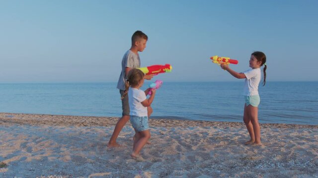 Little girls and boy on the sea. Children playing with water guns.
