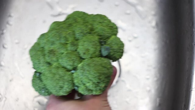 Washing broccoli in the kitchen sink. Close-up. Male hands wash fresh green broccoli in the kitchen sink.