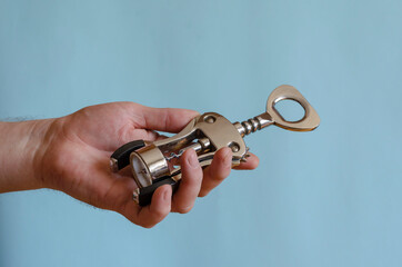 Adult man holds a metal corkscrew in his hand.