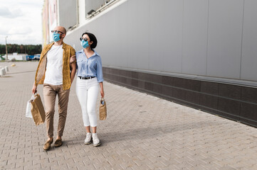 Shopping during quarantine. Couple in love in protective masks walking with paper bags near the mall wearing in a stylish casual wear and sunglasses